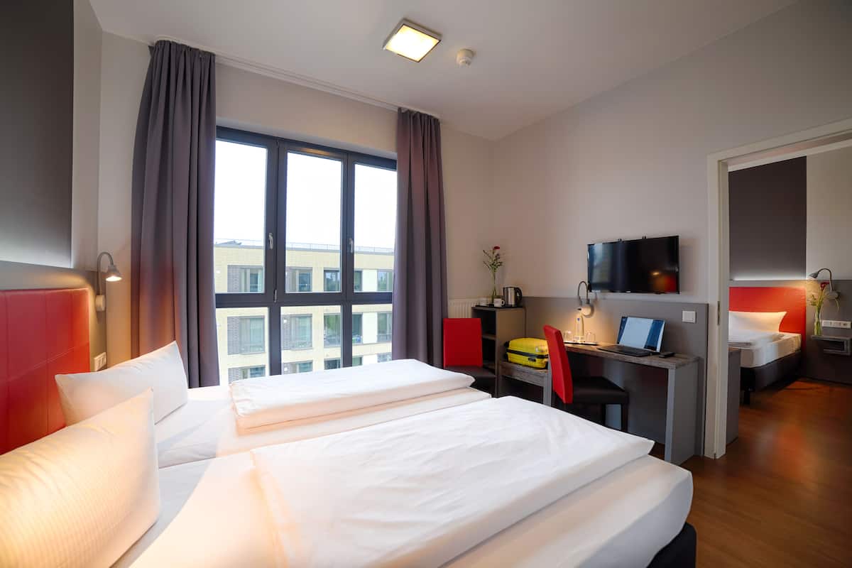 Een hotelkamer met twee bedden, een bureau met een laptop, een televisie en uitzicht op gebouwen.