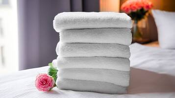 Un montón de toallas blancas sobre una cama con una rosa rosa a un lado.