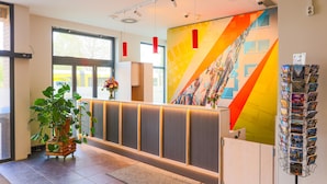Un espace d’accueil au design moderne, comprenant un comptoir d’accueil, une grande fresque murale aux couleurs vives et une plante.
