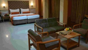 A hotel room with a large bed, two armchairs, a sofa, and a small table with fruit.