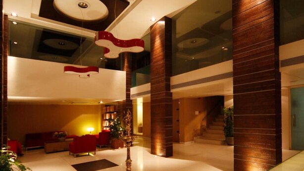 A modern hotel lobby with a central red and white sculpture, a glass coffee table with decorative items, and a staircase leading to upper floors.