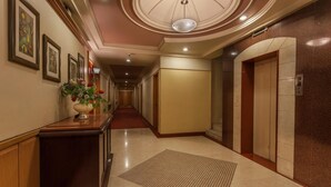 A hotel hallway with a wooden reception desk, framed artwork, a potted plant, and an elevator.