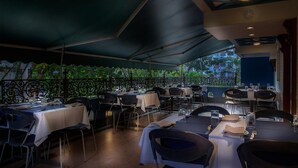 An outdoor dining area with tables and chairs, a covered section, and a view of buildings in the background.