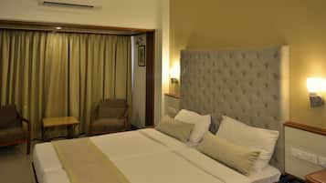 A hotel room with a large bed, two armchairs, a small table, a bedside lamp, and an air conditioning unit.