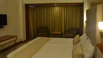 Una habitación de hotel con una cama grande, televisión, escritorio y una zona de estar con sillas y una mesa.