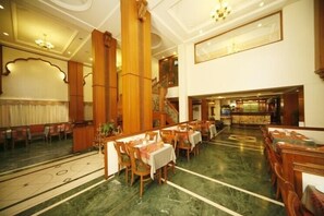 Un amplio vestíbulo de hotel con suelo de mármol, muebles de madera y una escalera que conduce a un nivel superior.