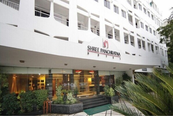 Un hotel llamado "Shree Panchratanahotel" con una fachada moderna, ventanas amplias y un área de entrada bien cuidada con escalones y plantas en macetas.