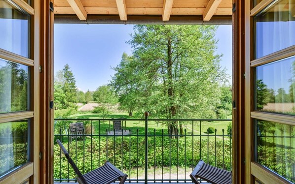Een balkon met uitzicht op een park, een houten pergola en twee houten stoelen.