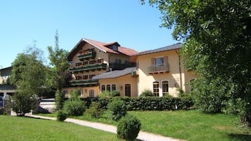 A two-story building with a yellow facade, multiple balconies with flower boxes, and a gravel path leading to the entrance.