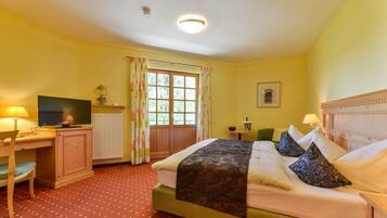 Ein Hotelzimmer mit Bett, Schreibtisch mit Fernseher, Stuhl, Fenster mit Vorhängen und Heizkörper.