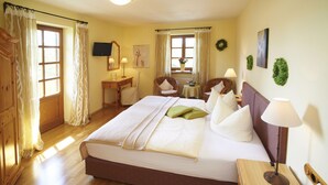 A hotel room with a large bed, wooden floor, a desk with a chair, a small table with a lamp, and a television on the wall. - Hotel Gasthof Oberwirt (Obing)