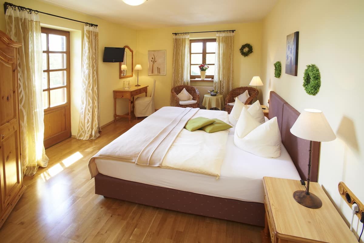 Een hotelkamer met een groot bed, houten vloer, bureau met stoel, een kleine tafel met lamp en een televisie aan de muur.