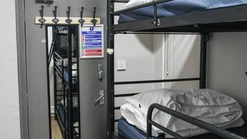 Camera con un letto a castello, una porta metallica, un'uscita di sicurezza e un piccolo spazio contenitore.
