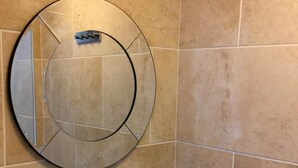 A bathroom with a round mirror, a smoke detector, and beige tiles. - Onefam Waterloo 18-36 years old (London)
