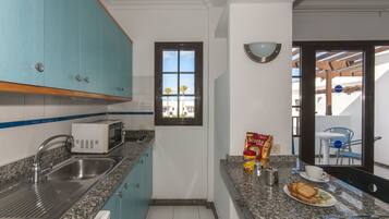A compact kitchen with a built-in microwave, a sink, and a window overlooking a balcony.
