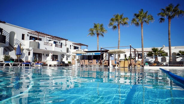 A pool area with lounge chairs, a snack bar, and palm trees. - Apartamentos Plaza Azul (Tías)