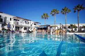 A pool area with lounge chairs, a snack bar, and palm trees. - Apartamentos Plaza Azul (Tías)