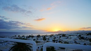 A coastal town at sunset with white buildings and palm trees. - Apartamentos Plaza Azul (Tías)