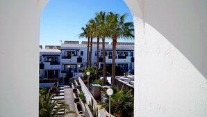 A view through an archway of a hotel with multiple floors, palm trees, and a clear blue sky. - Apartamentos Plaza Azul (Tías)