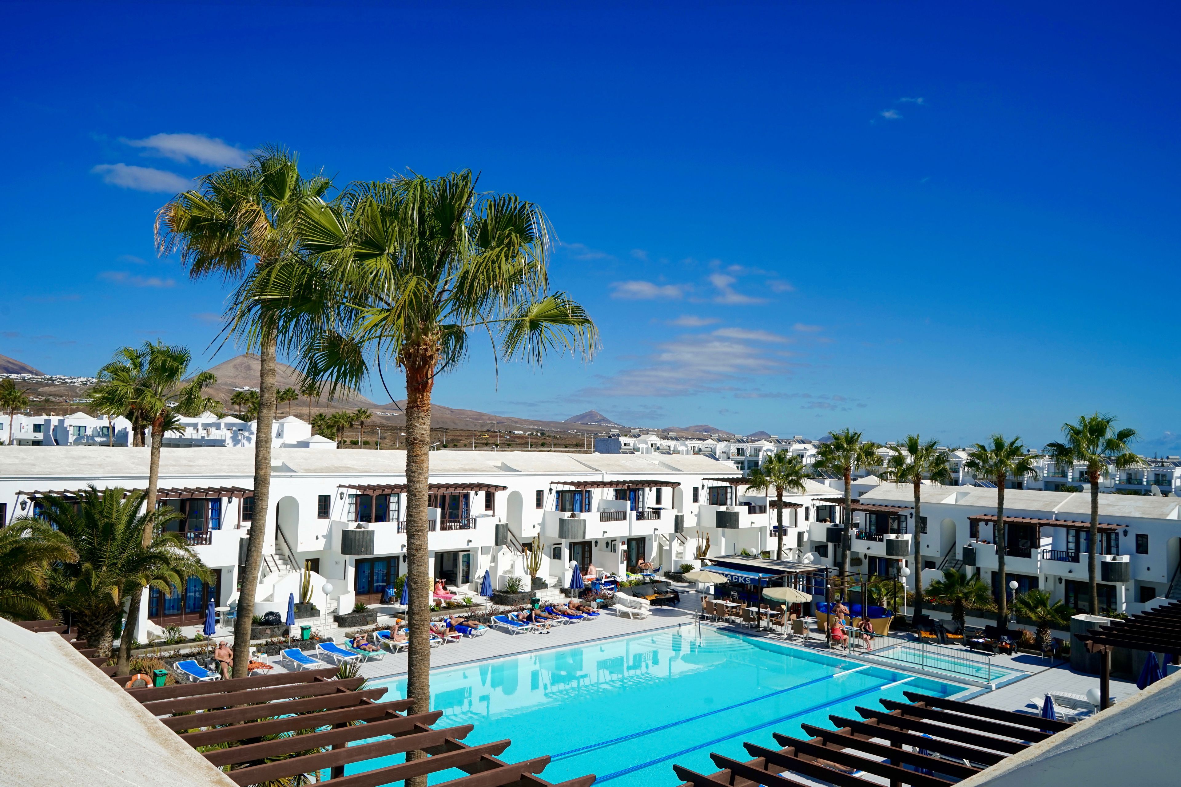 A resort with a pool, palm trees, and white buildings with balconies.
