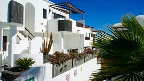 A white building with balconies, a pergola, and a sign indicating a pedestrian path. - Apartamentos Plaza Azul (Tías)