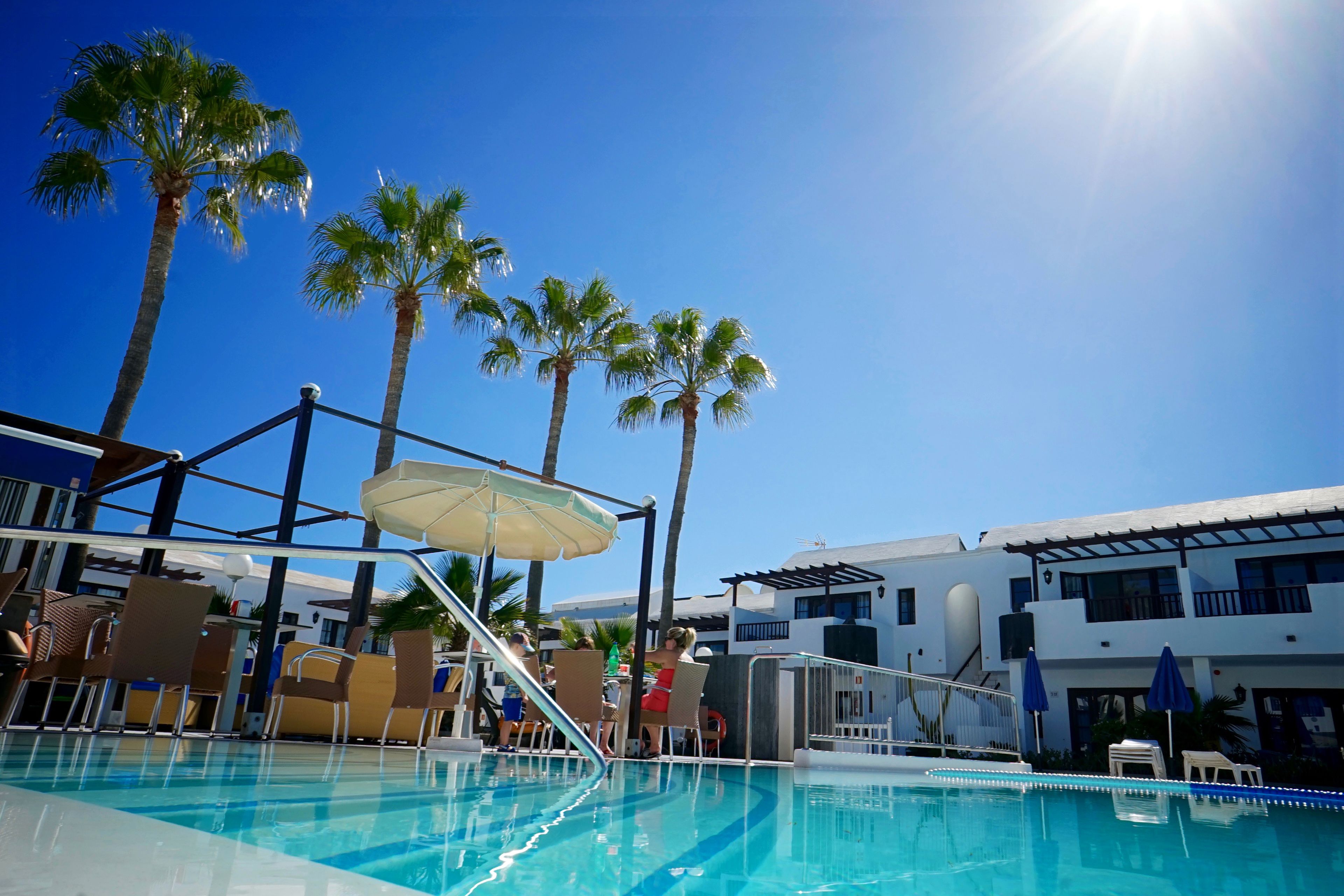 Un área de piscina con sillones de descanso, sombrillas y palmeras.