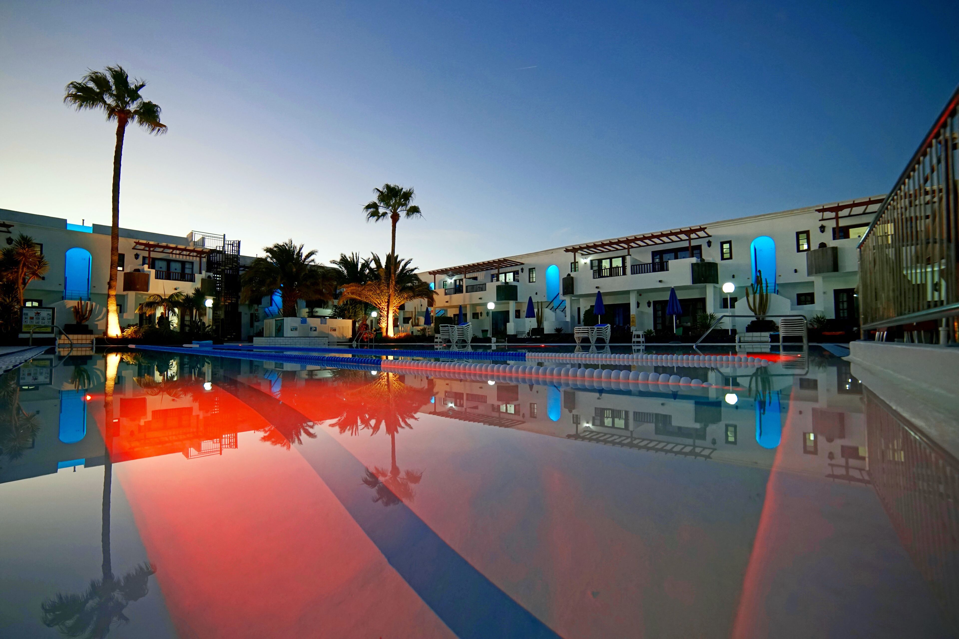 A hotel with a swimming pool, palm trees, and a clear sky.