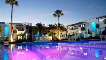 A hotel with a swimming pool, palm trees, and modern architecture.