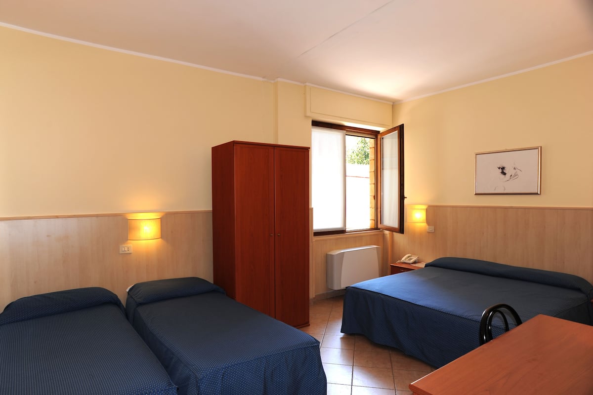 A room with two single beds, a wooden wardrobe, a radiator, and a framed picture on the wall.