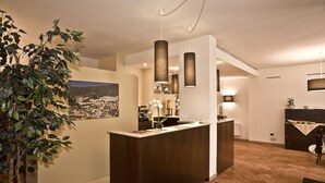 A modern reception area with a wooden reception desk, pendant lighting, and a large potted plant. - Villa Santa Croce (San Giovanni Rotondo)