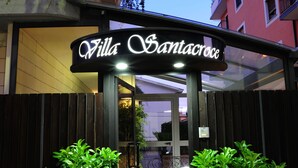 The entrance to Villa Santacroce with a sign above the door, potted plants on either side, and a red carpet leading inside. - Villa Santa Croce (San Giovanni Rotondo)
