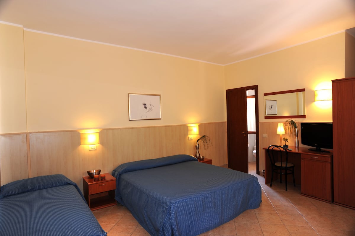 A hotel room with two beds, a desk with a chair, a television, and a mirror.