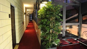 A corridor with a red carpet, a large bamboo plant, and a seating area with red cushions. - Villa Santa Croce (San Giovanni Rotondo)