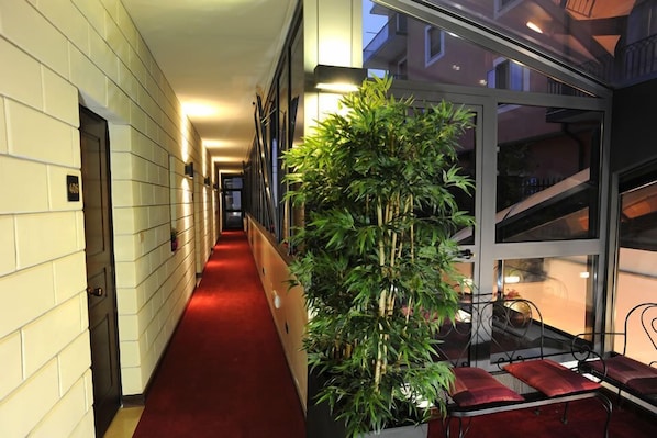A corridor with a red carpet, a large bamboo plant, and a seating area with red cushions.