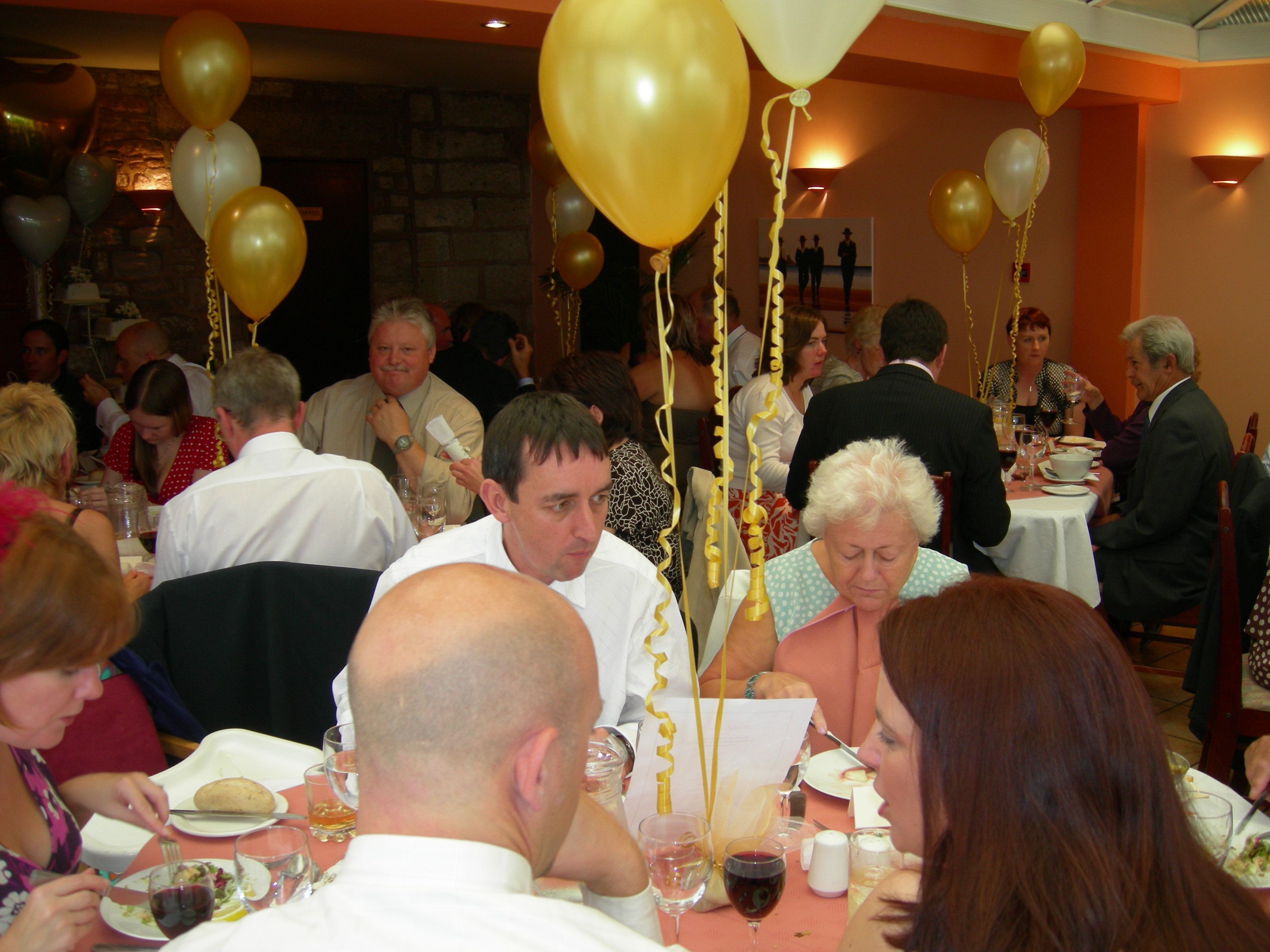 A crowded indoor dining area with tables set for meals, surrounded by balloons.