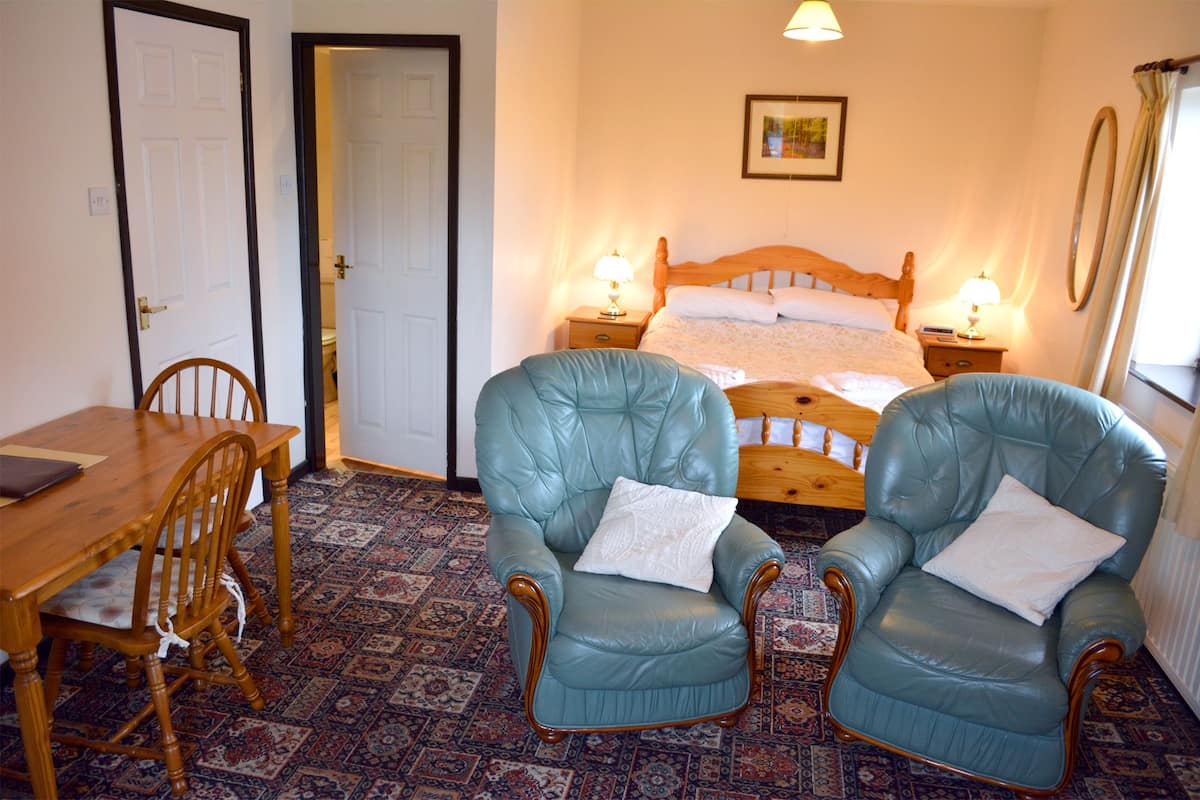 A room with a wooden bed, two blue armchairs, a wooden table, and a patterned carpet.