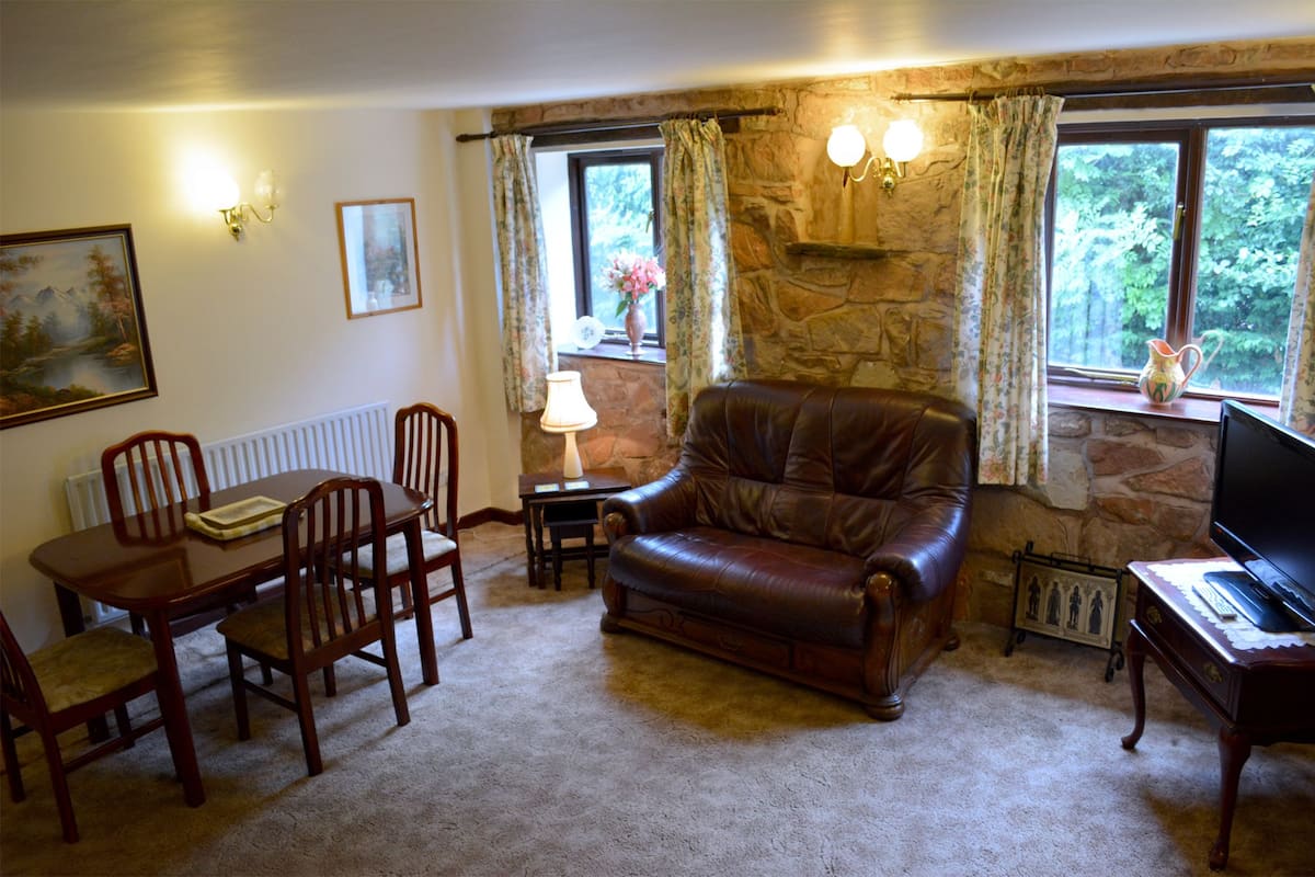 A cozy living room with a stone fireplace, a leather sofa, a dining table with chairs, and a television.