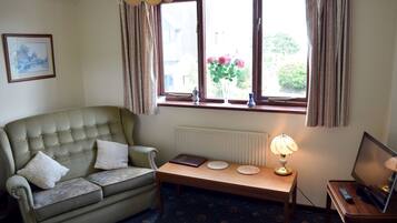 A living room with a green sofa, a small table with a lamp, and a window with curtains.