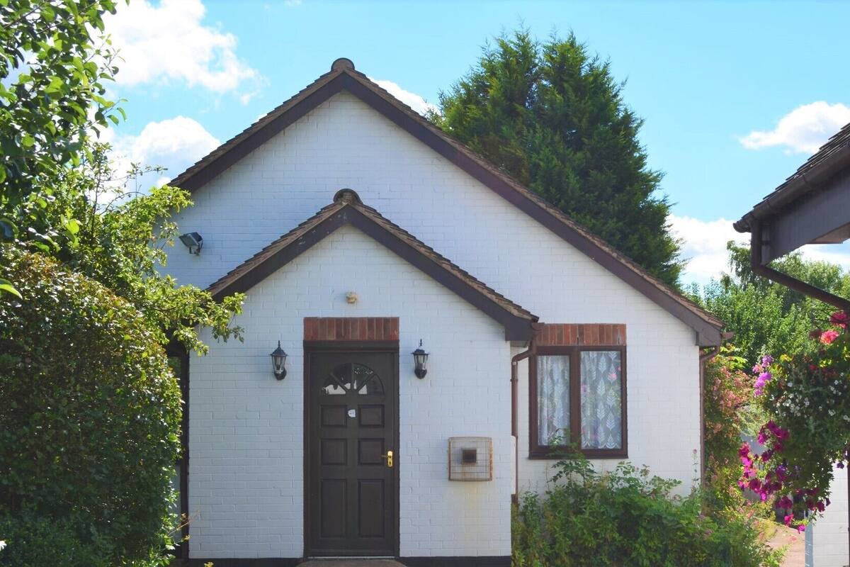 A white brick house with a dark brown door, two windows with shutters, and a small porch area.