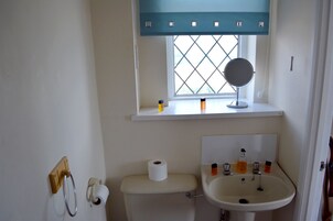 A bathroom with a toilet, a sink, a window with a mirror, and toiletries on the windowsill.