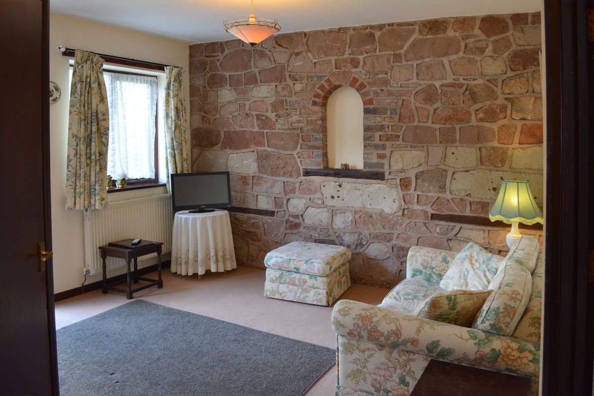 A cozy living room with a stone fireplace, a television on a small table, a sofa, and a lamp.