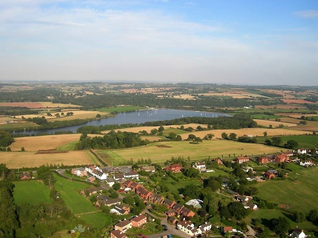An aerial view of a rural village with houses, fields, and a lake.