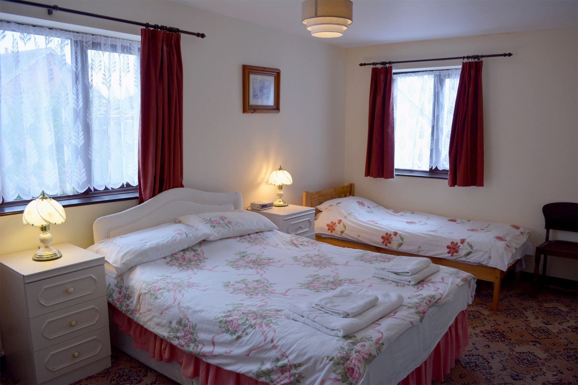 Ein Zimmer mit zwei Betten, jeweils mit floralem Bettzeug, einem Nachttisch mit Lampe und einem Sessel.