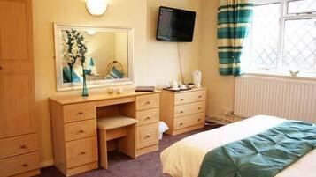 A bedroom with a bed, a desk, a mirror, a television, and a window with curtains.