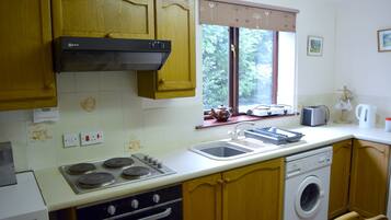 A kitchen with wooden cabinets, a stove, a sink, a window with a view of greenery, and a washing machine.
