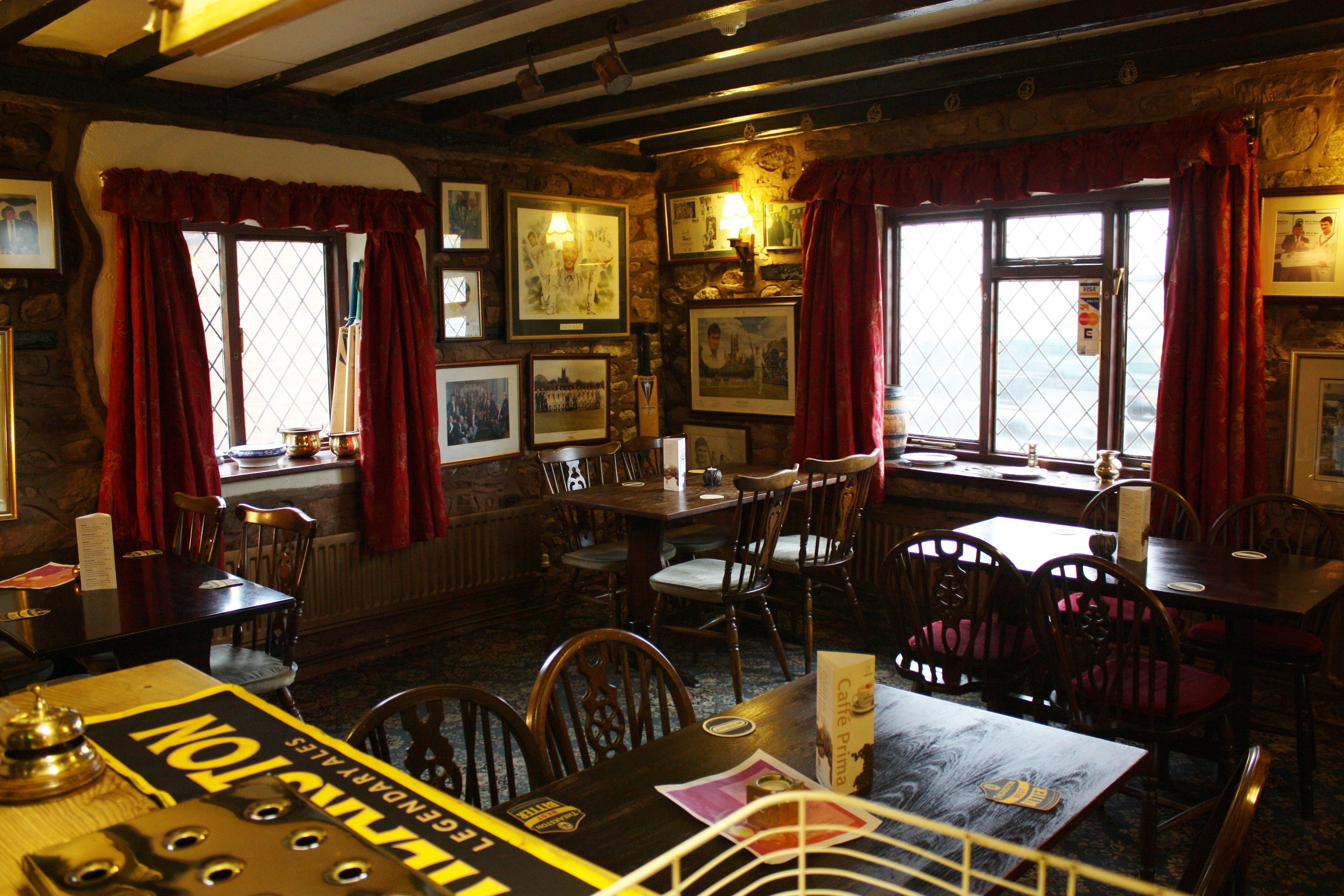 Un restaurante acogedor con muebles de madera, cuadros en las paredes y ventanas amplias con cortinas rojas.