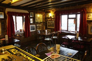 Un restaurante acogedor con muebles de madera, cuadros en las paredes y ventanas amplias con cortinas rojas.