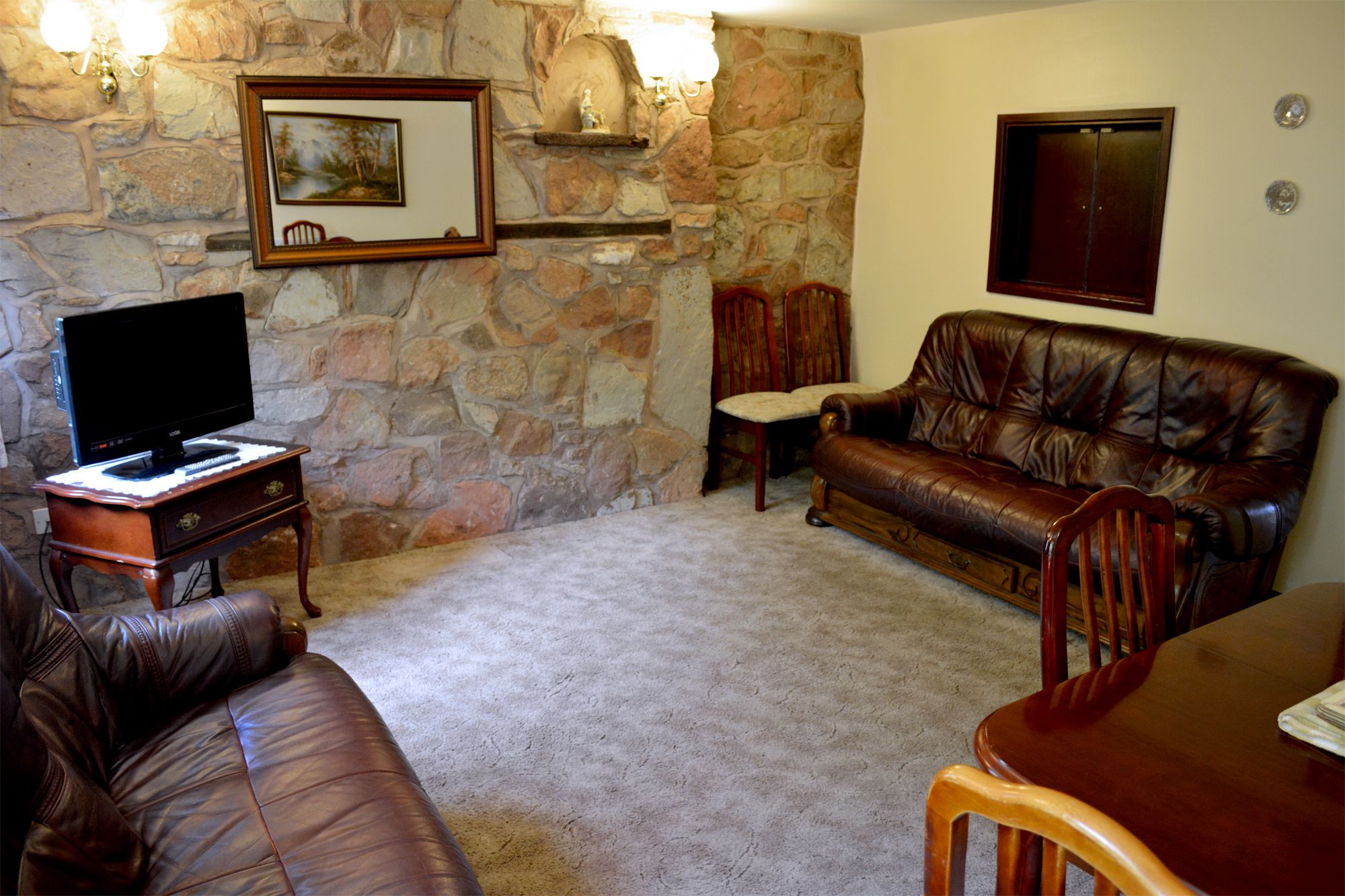 Ein Wohnzimmer mit Steinsandsteinwand, einem Fernseher auf einem Holzständer, einem Ledersofa, einem Holztisch und einem Kamin.
