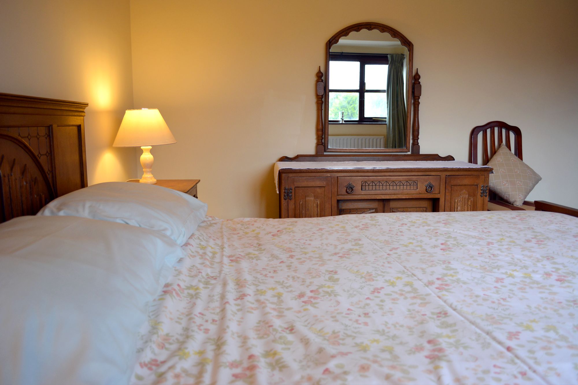 Un dormitorio con cama, cómoda, espejo y mesita de noche con lámpara.