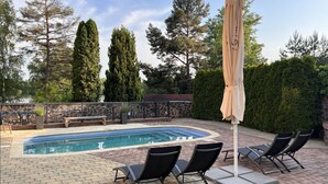A swimming pool with lounge chairs and an umbrella, surrounded by trees and a stone wall. - Resort-Restaurant Štilec (Kamenný Újezd)